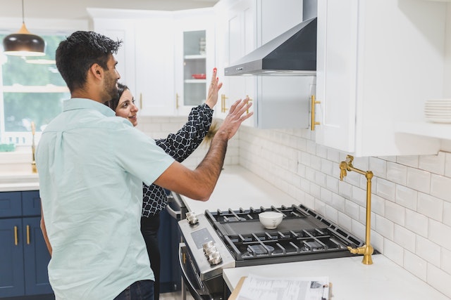 Two people in a white kitchen looking at a black stovetop and its accompanying features